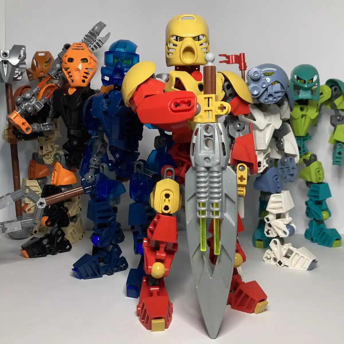 A group of colorful Bionicle action figures are posed together against a plain white background, with one large yellow…