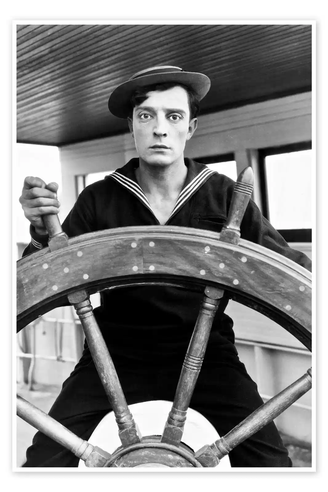 A black-and-white photo shows a man in a sailor uniform and hat gripping a ship's wheel, looking intensely forward. The…