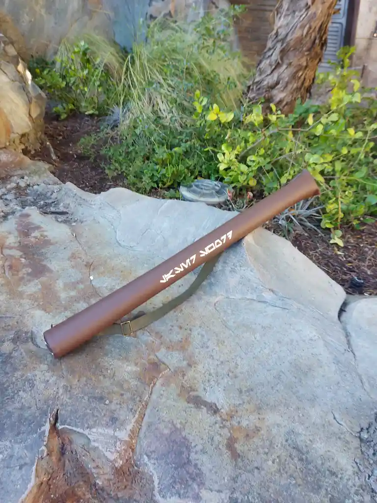 A brown cylindrical case with white text reading 'JKVM7 YOOP77' lies diagonally on a large, textured rock outdoors…