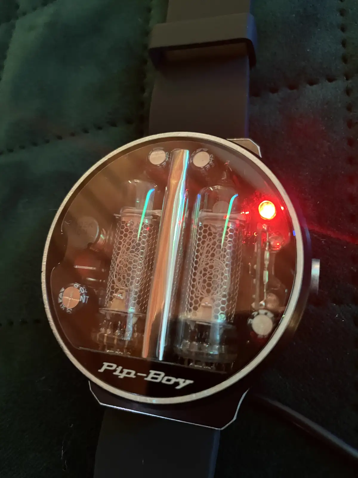 A close-up of a wristwatch with a transparent face revealing glowing vacuum tubes and circuitry inside, resembling a Pip-Boy…