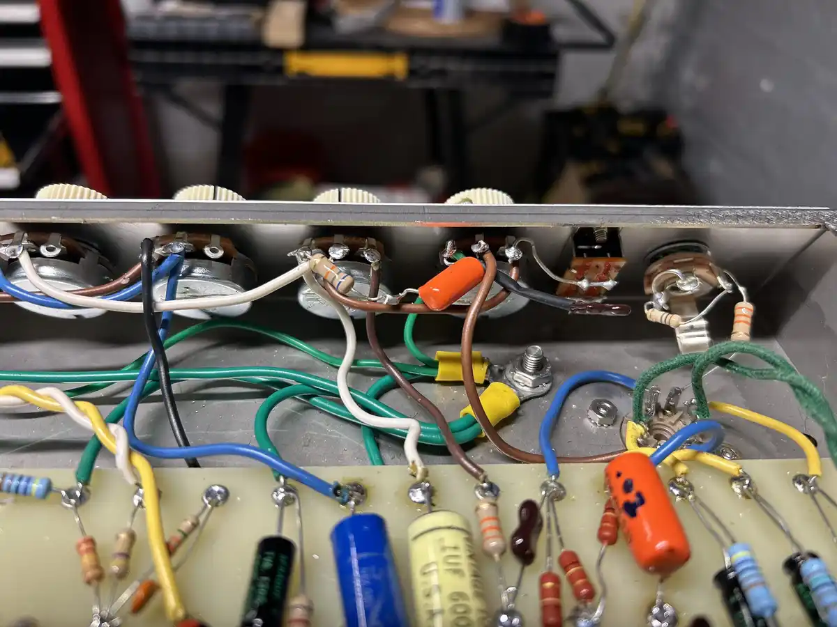 A close-up photo of a densely wired electronic circuit board with colorful wires, resistors, capacitors, and knobs, showing…