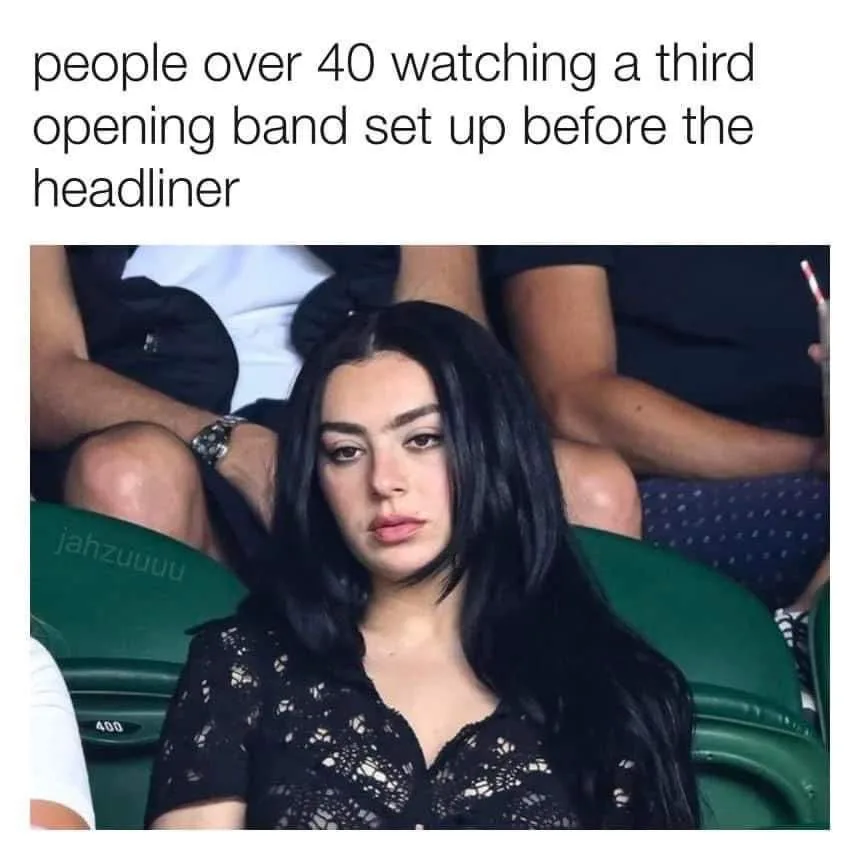 A woman with long black hair and a black lace top sits in a green stadium seat, looking bored and unimpressed. The text…