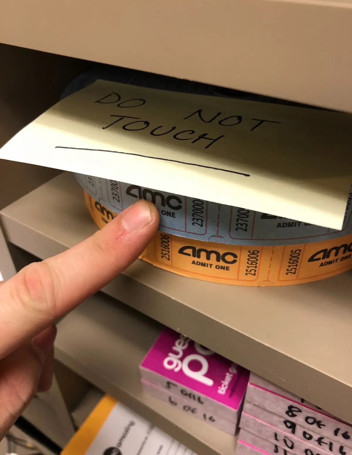 A close-up photo shows a person's finger pointing at a roll of AMC movie tickets on a shelf. A handwritten sticky note…