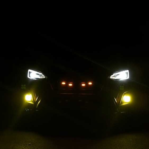 A nighttime photo of a car's front view, with its headlights and fog lights illuminated against a dark background. The car's…