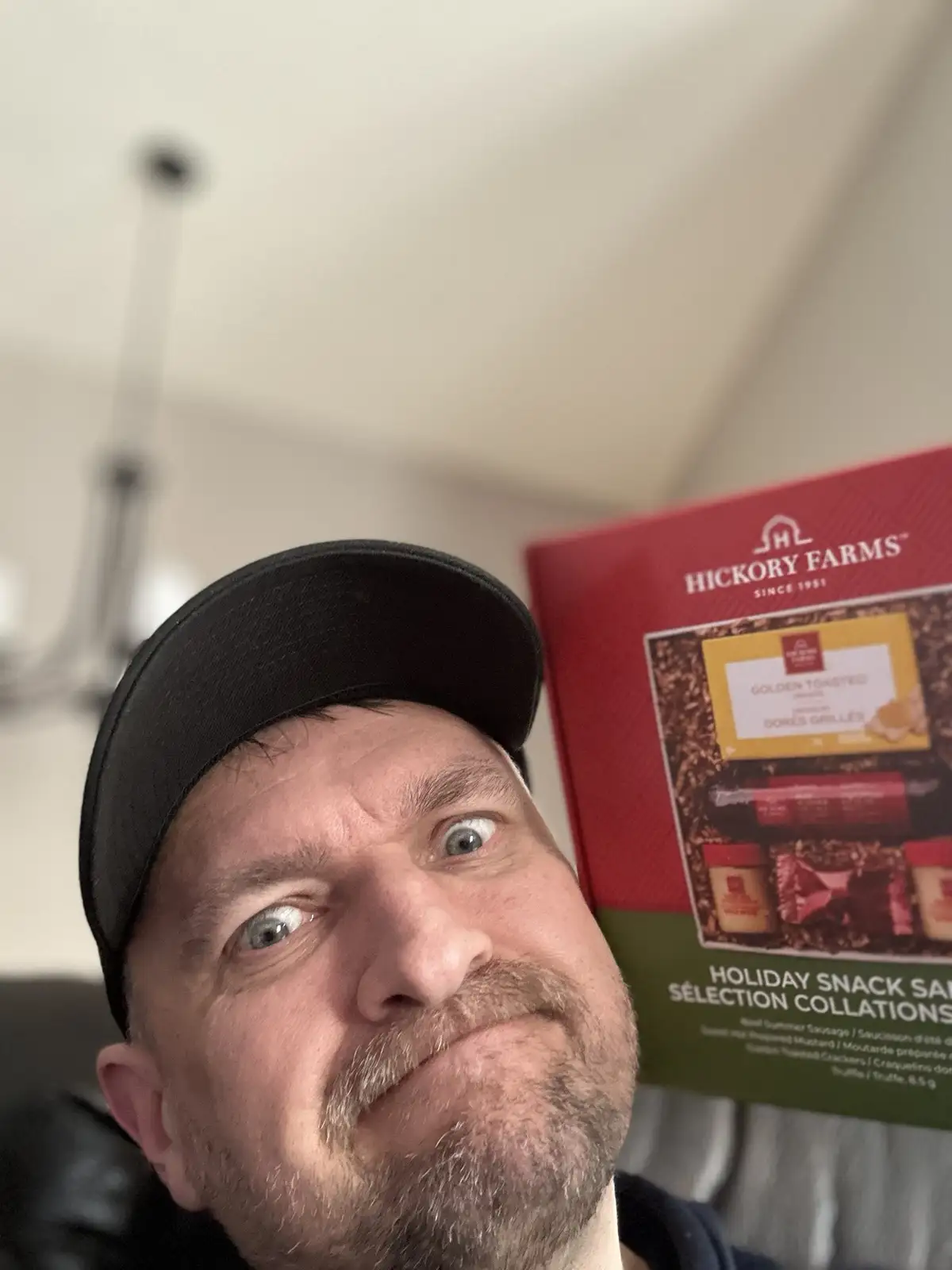 A man with a black baseball cap and a surprised, wide-eyed expression looks at the camera while holding a red and green…