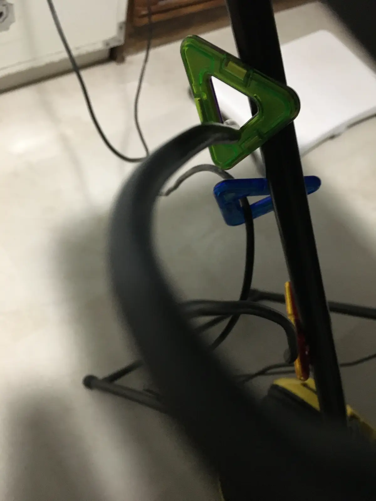 A blurry photo shows a black cable organizer stand with colorful plastic clips holding black cables. A large black cable is…
