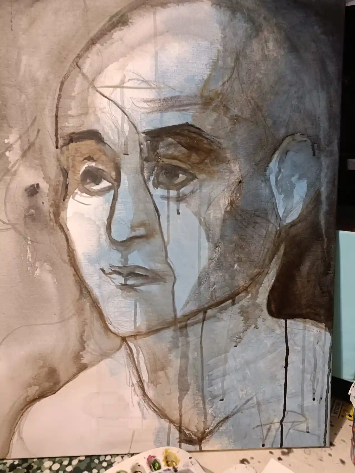 A watercolor painting on canvas depicts a single face with a tear falling from one eye, rendered in muted browns and blues…
