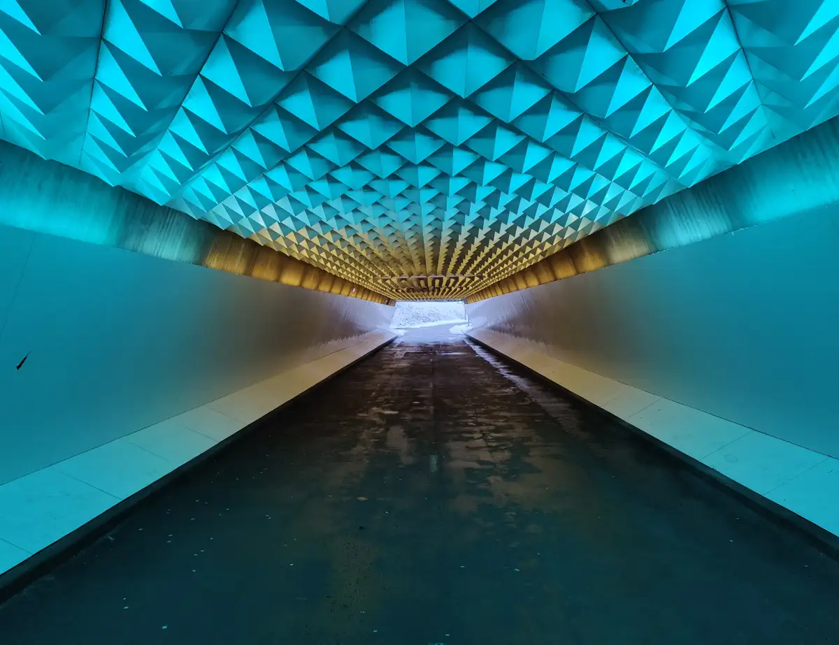 A low-angle shot looking down a long, modern tunnel with a ceiling composed of repeating blue and gold triangular panels…
