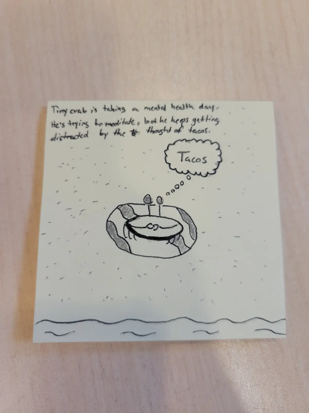 A hand-drawn sketch on a sticky note shows a tiny crab sitting cross-legged in a meditative pose on a sandy ocean floor. A…