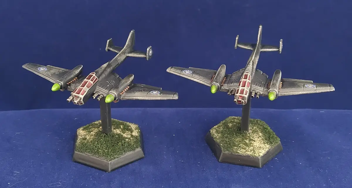 Two identical gray model airplanes with green engine nacelles and red-tinted cockpit canopies are mounted on hexagonal bases…