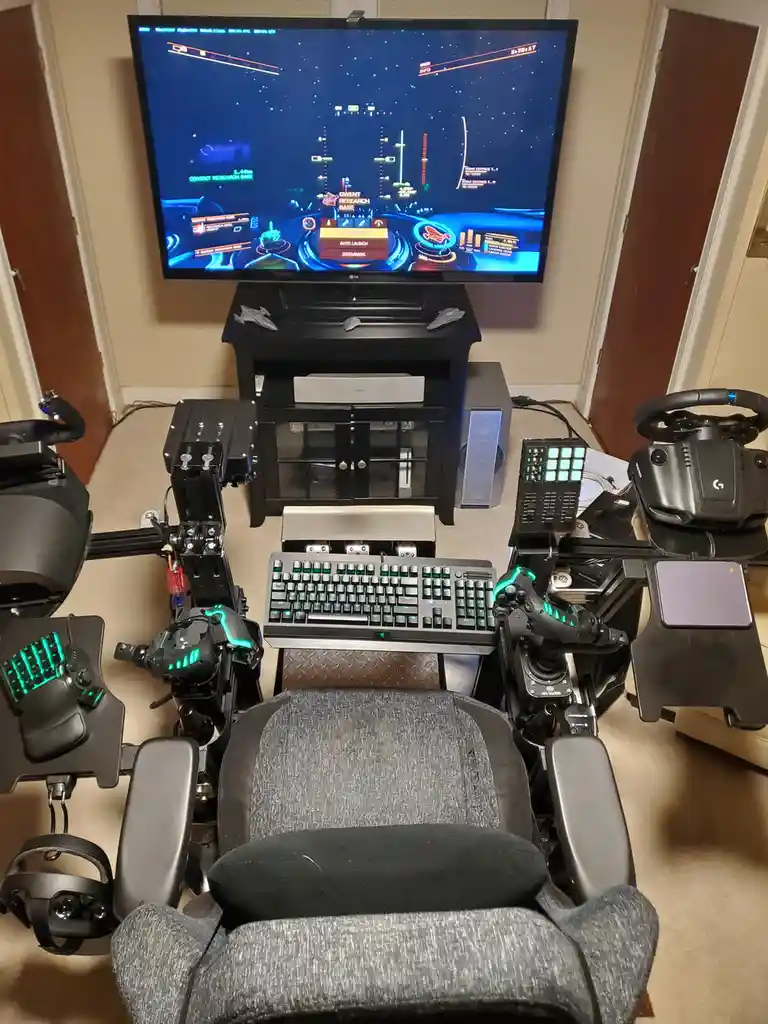 An overhead view of an elaborate, custom-built gaming cockpit setup featuring a large TV displaying a space combat game, a…