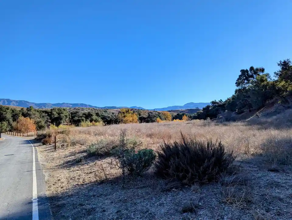 A scenic photo of a paved road curving through dry, grassy hills under a clear blue sky, with distant mountains and…
