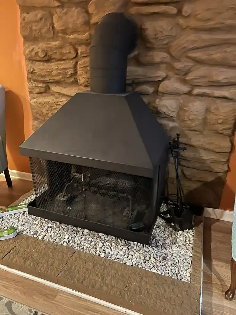 A modern black metal fireplace insert is installed within a stone fireplace surround, set on a bed of white gravel. The…