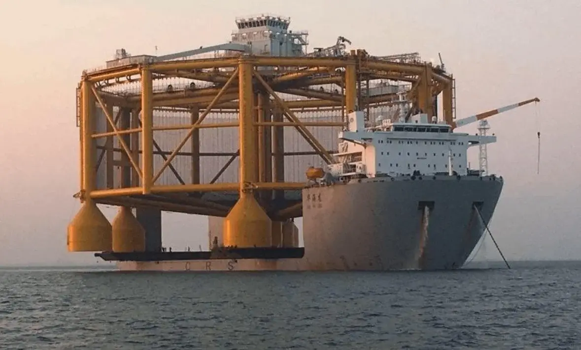 a large gray vessel with a massive yellow steel structure, resembling an offshore platform or heavy-lift crane, mounted on…