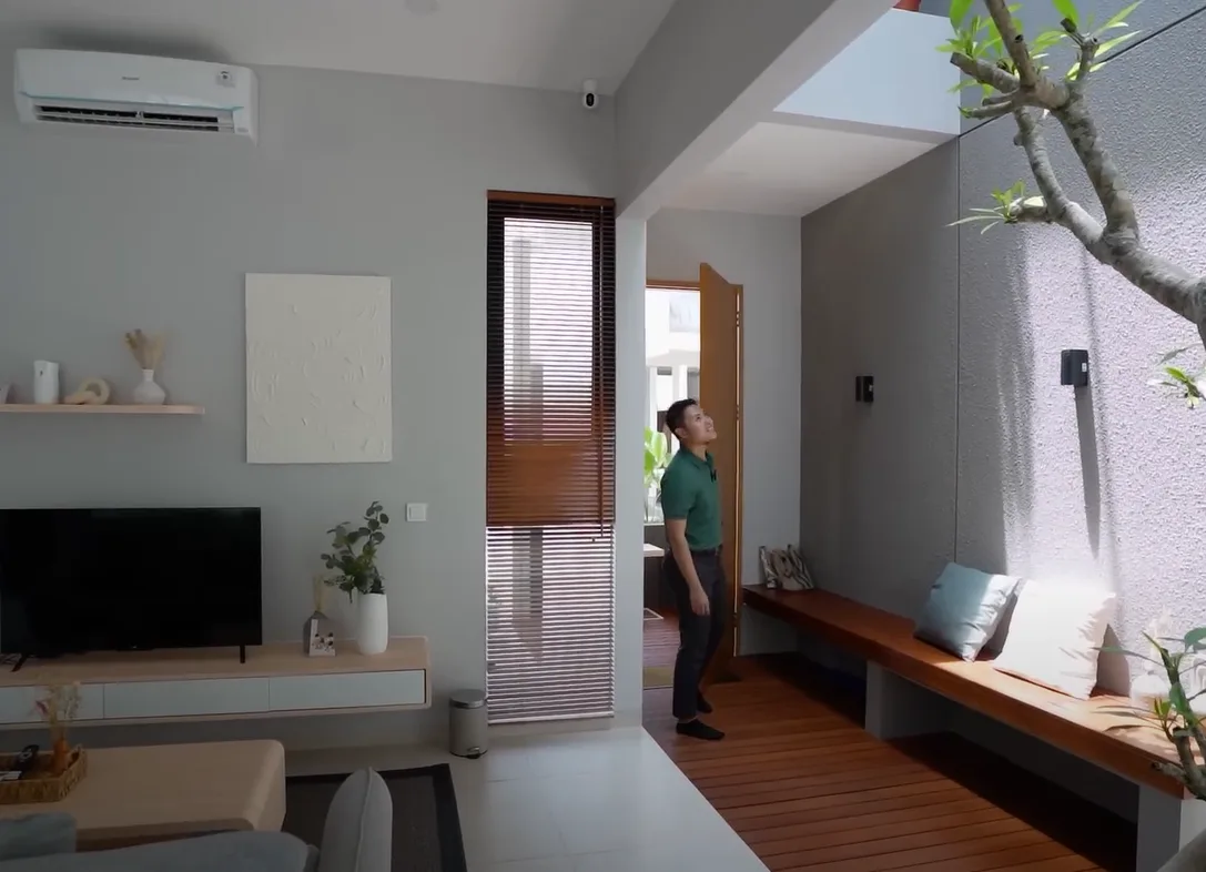 A man in a green polo shirt stands in a modern, minimalist living room with wooden floors and light gray walls, looking…