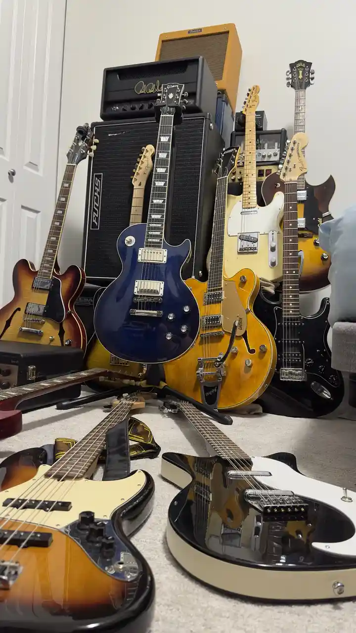 A room filled with numerous electric guitars of various colors and models, leaning against and stacked on large amplifier…