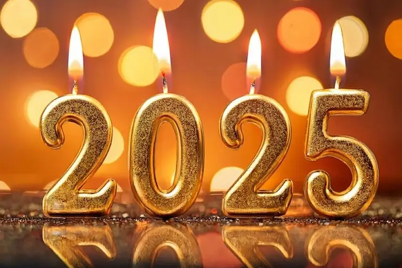 Four golden, glittery candles shaped like the numbers '2025' are lit with flames, standing on a reflective surface against a…