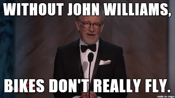 A man in a black tuxedo with a bow tie and glasses stands at a podium, smiling slightly. White bold text overlays the image…