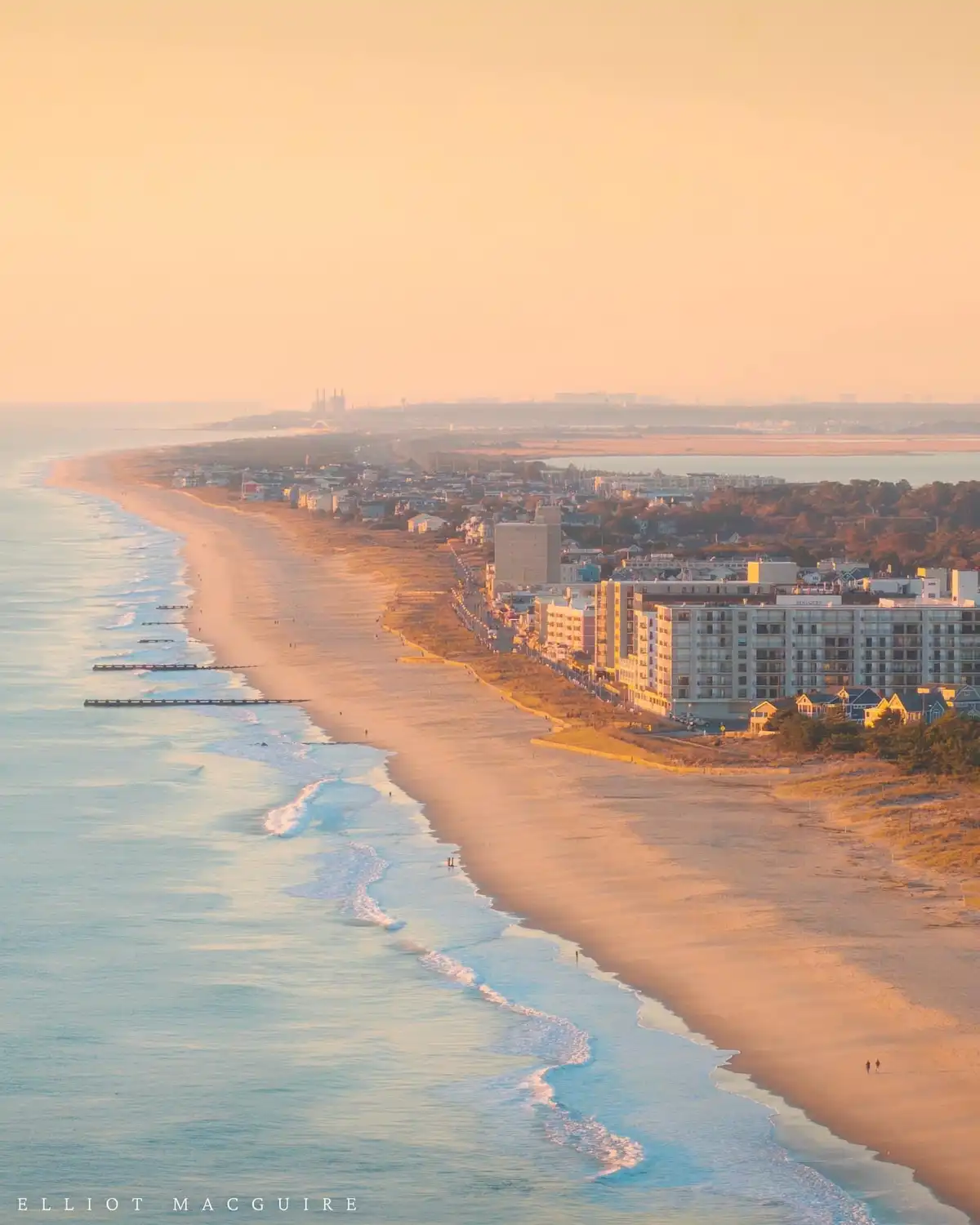 A serene, wide-angle photograph of a beach at sunrise or sunset, with golden light bathing the sand, ocean waves, and…