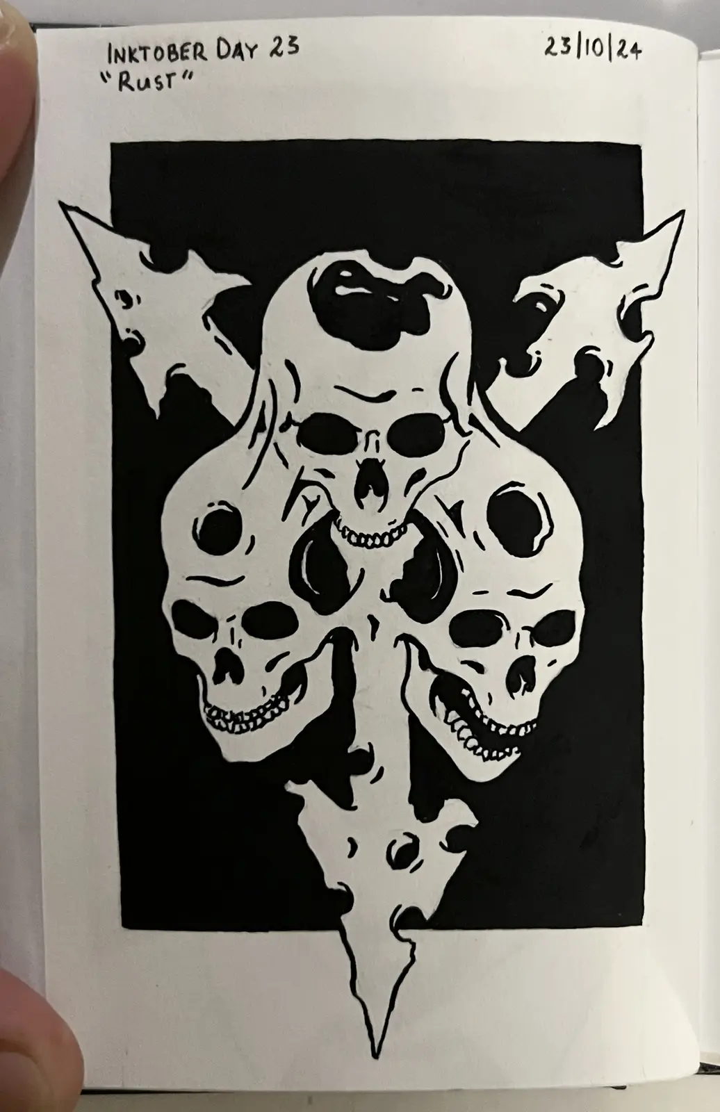 A black-and-white ink drawing on paper shows three skulls arranged in a triangular formation against a black background…