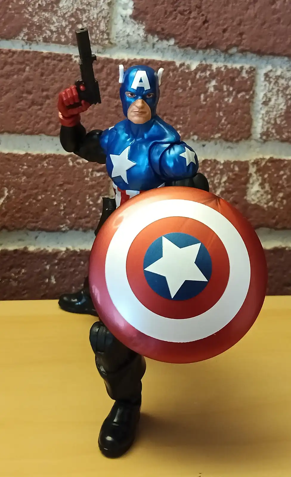 A Captain America action figure stands in a heroic pose against a brick wall, holding his iconic round shield in front of…