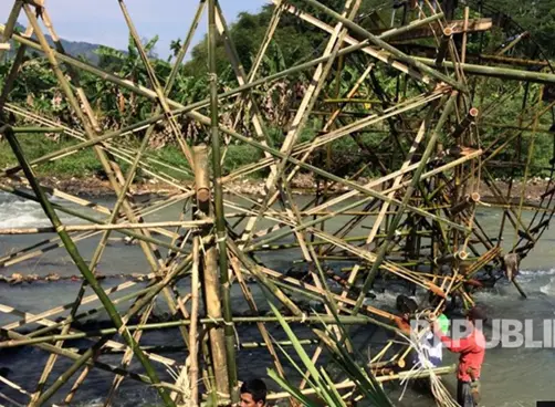a large, complex bamboo structure resembling a giant wheel or scaffold is being constructed over a river, with several…