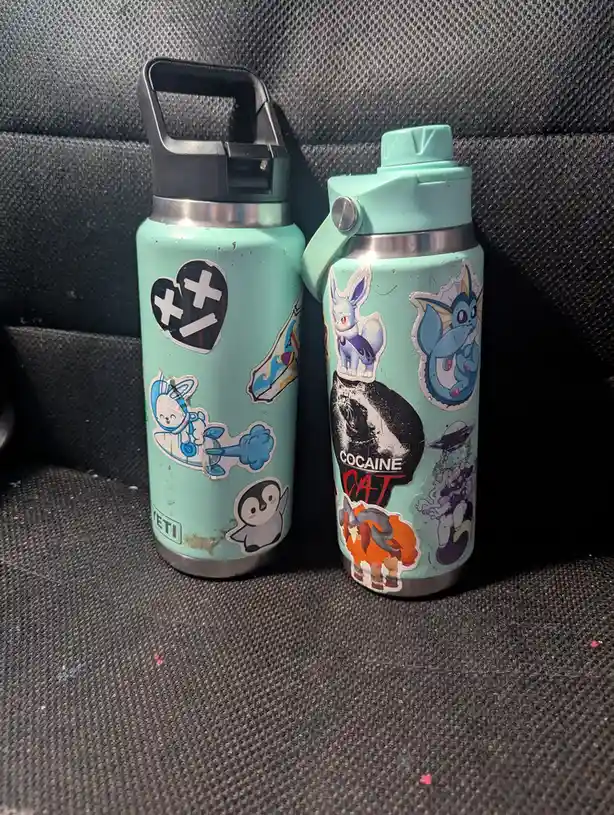Two mint green water bottles, one with a black lid and one with a mint lid, sit side by side on a dark textured car seat…
