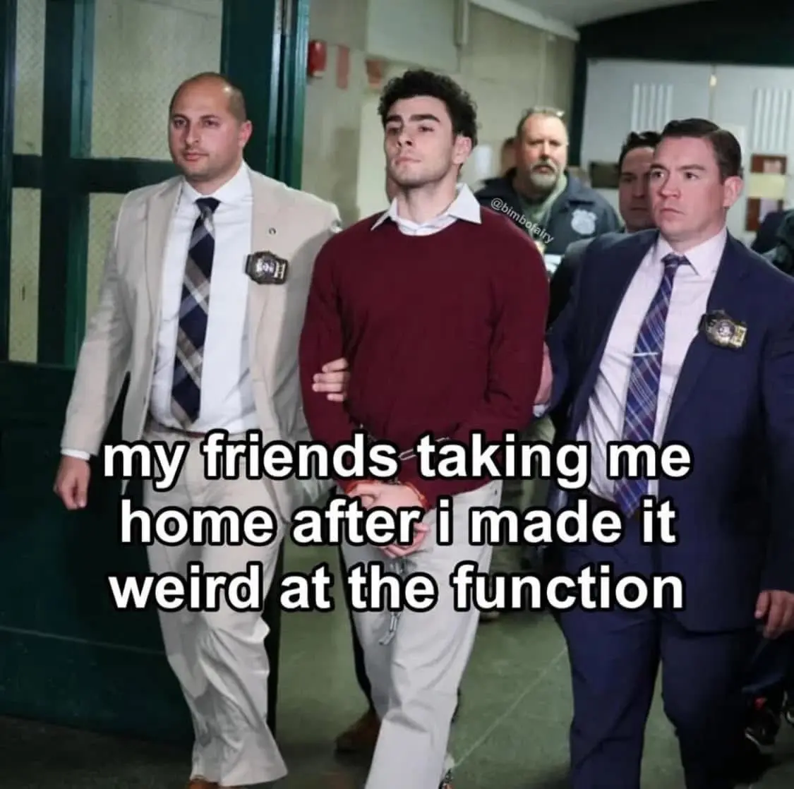 A man in a maroon sweater is being escorted by two uniformed officers through what appears to be a courthouse or police…