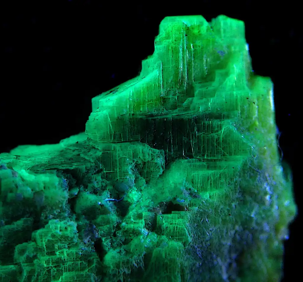 a close-up photograph of a vibrant green, fluorescent mineral crystal formation against a black background, with layered…
