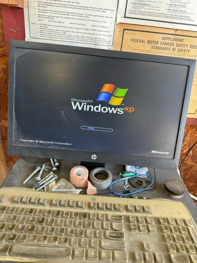 A dusty, old HP computer setup with a monitor displaying the Windows XP startup screen and a keyboard covered in grime…