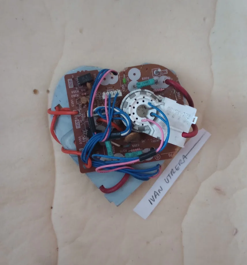 A close-up photo shows a disassembled electronic circuit board shaped like a heart, with colorful wires tangled around it…