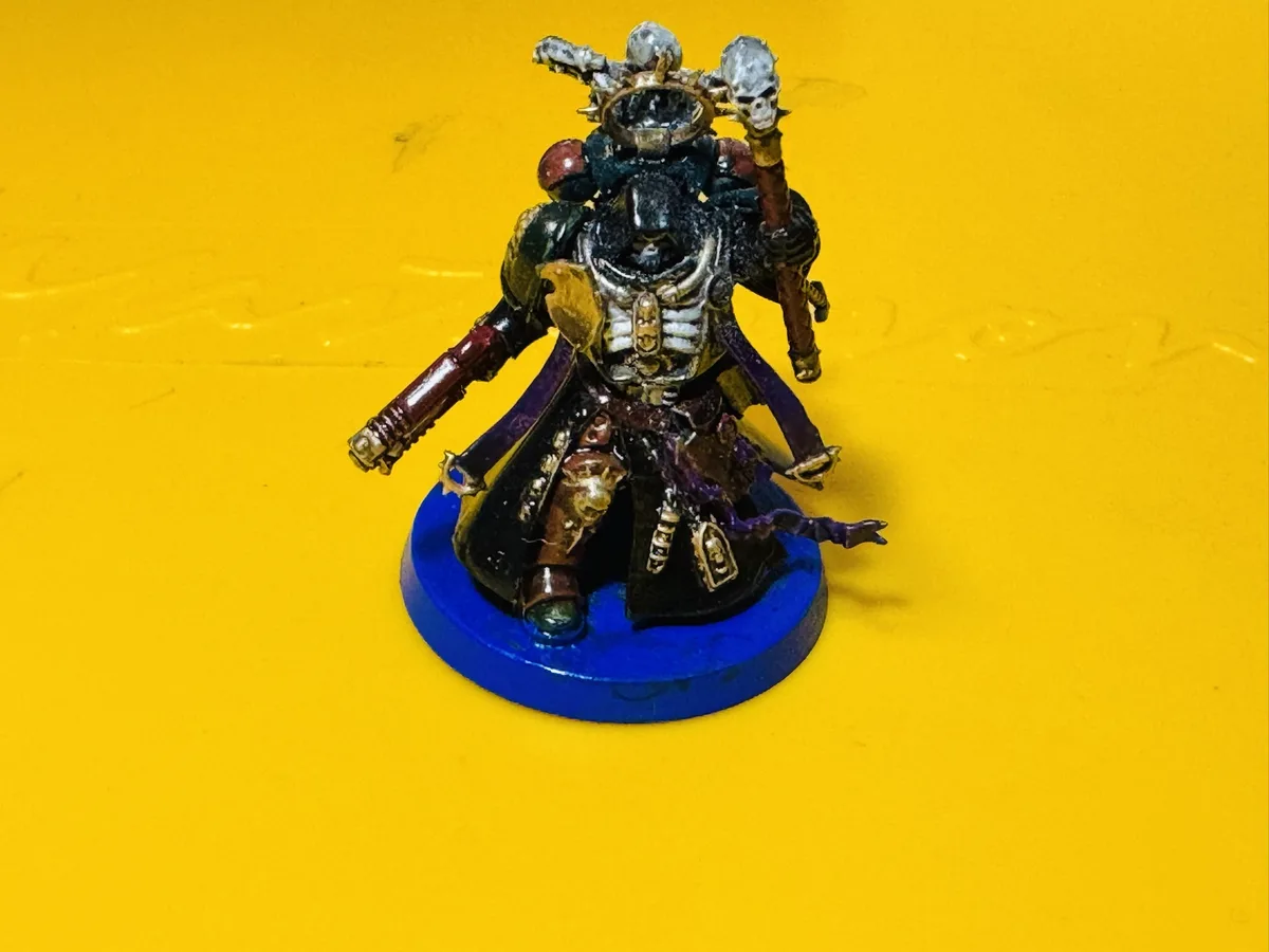A heavily painted miniature figure of a grimdark fantasy warrior, adorned with skulls, armor, and a purple cape, stands on a…