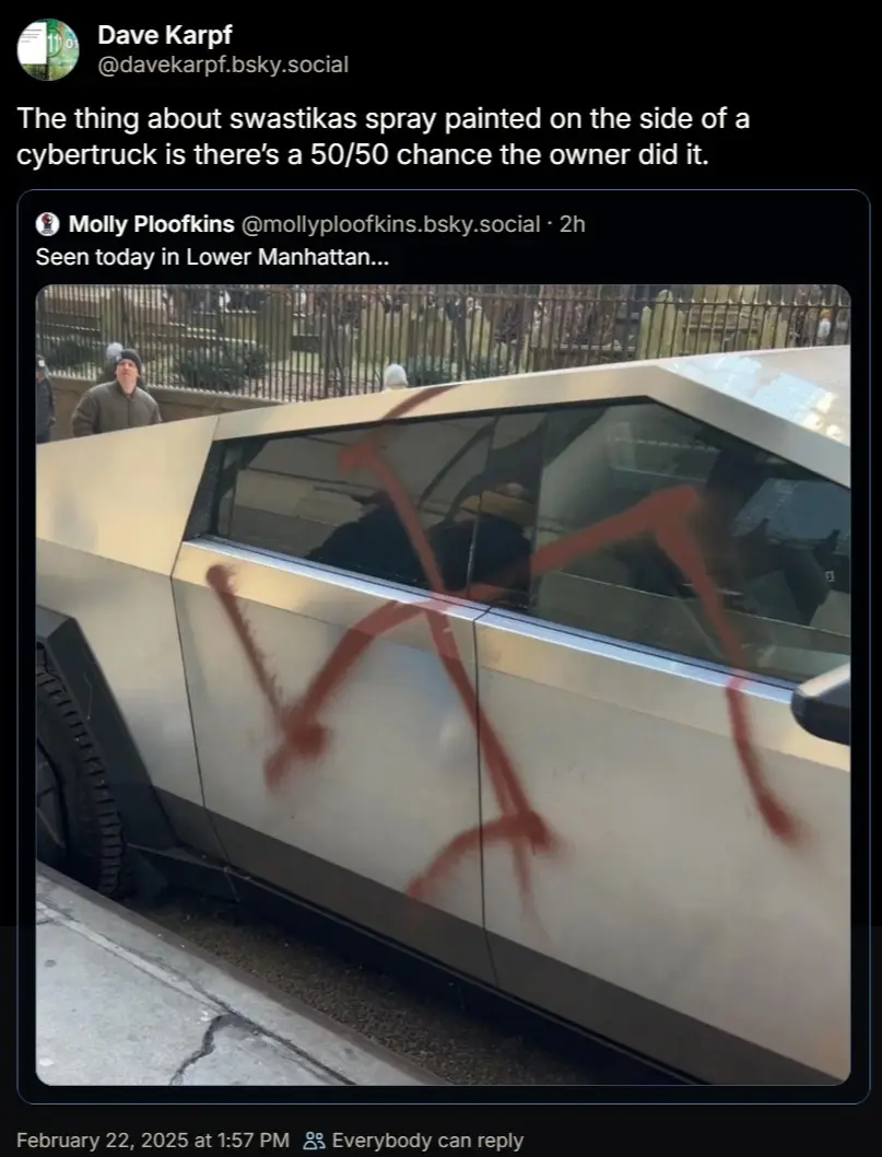 A silver Tesla Cybertruck is parked on a city street with a large, crudely spray-painted swastika visible on its side panel…