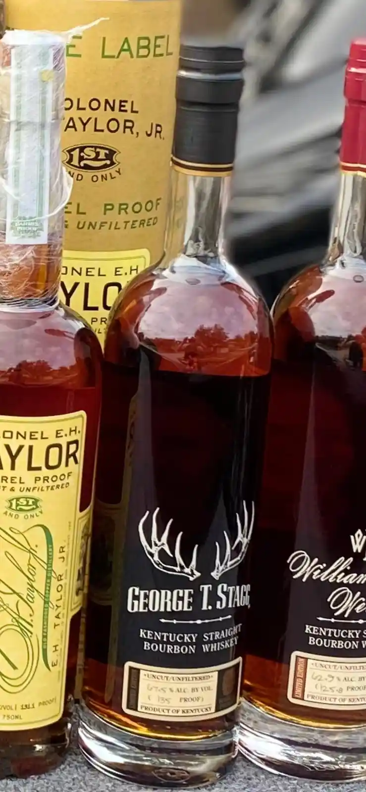 Three bottles of high-proof Kentucky bourbon whiskey are displayed side-by-side, with the central bottle labeled 'George T…