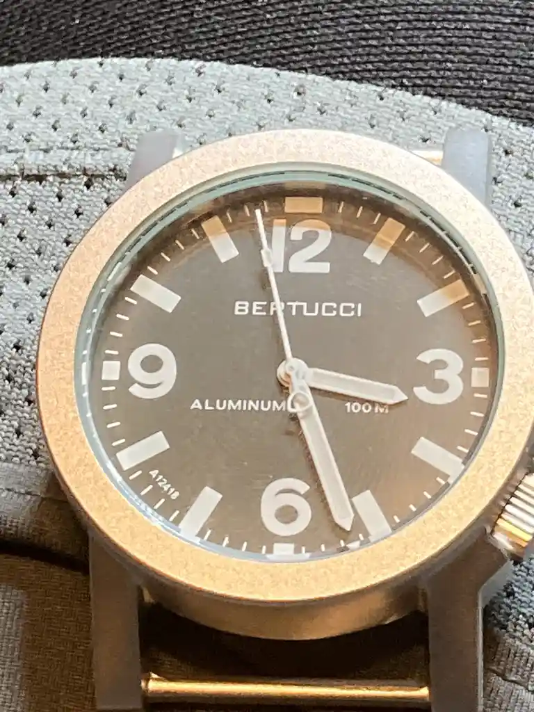 A close-up photo of a Bertucci brand watch with a bronze-colored case and a dark brown dial, featuring large white numerals…