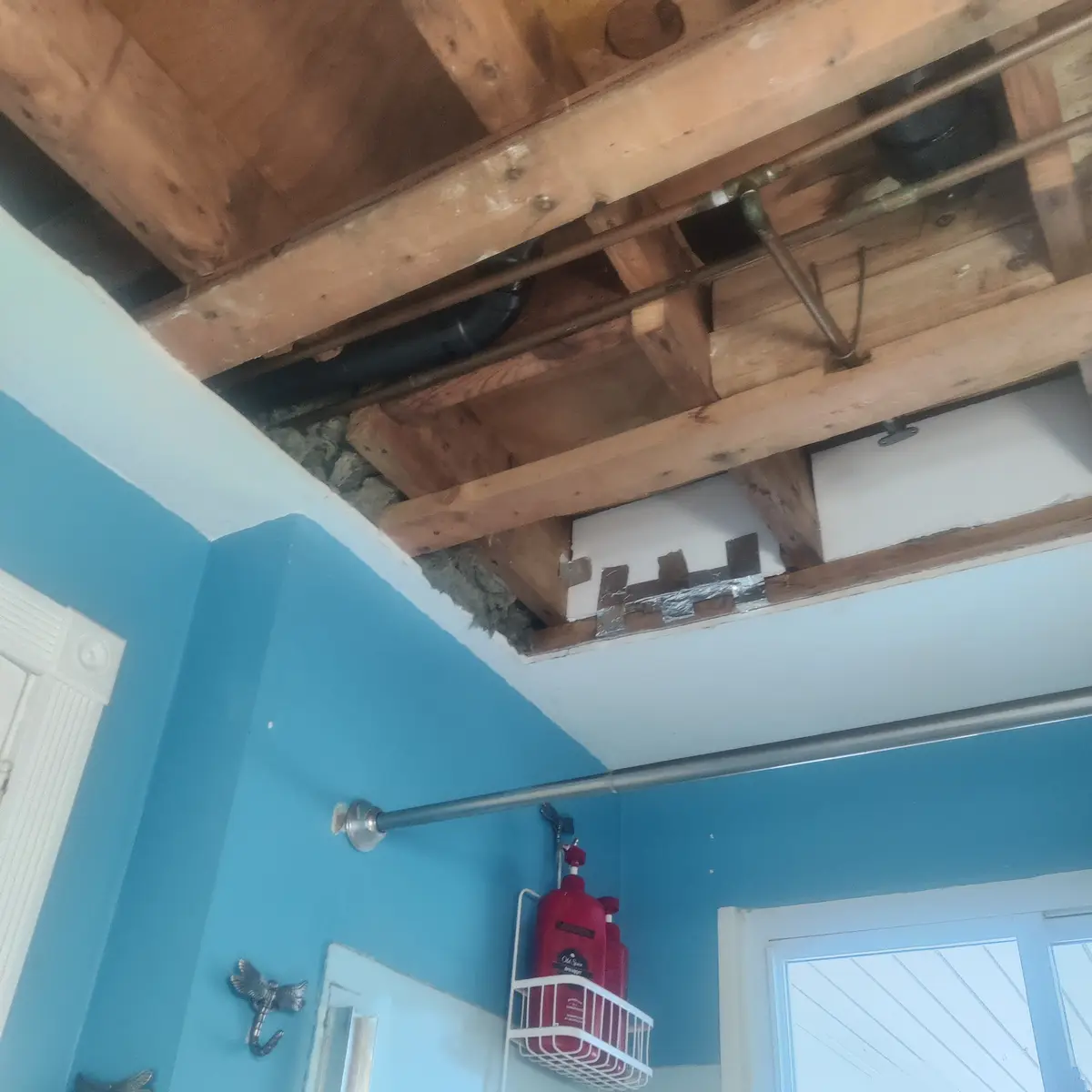 A bathroom ceiling is visibly damaged with exposed wooden beams, pipes, and insulation. The text overlay reads 'i just fixed…
