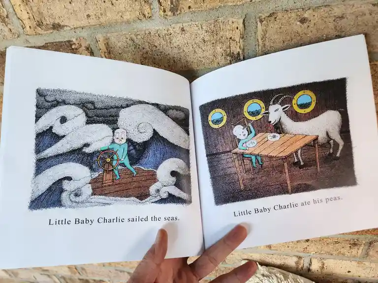 An open children's book shows two pages: left, a baby in a blue onesie steers a ship through stormy seas; right, the same…
