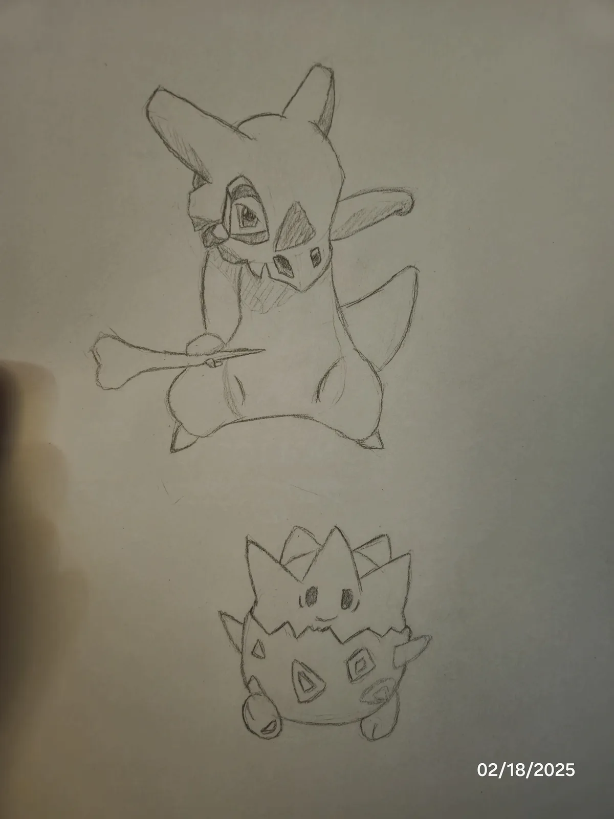 A pencil sketch on paper shows two Pokémon: a larger, fox-like creature holding a bone above a smaller, spiky, egg-shaped…