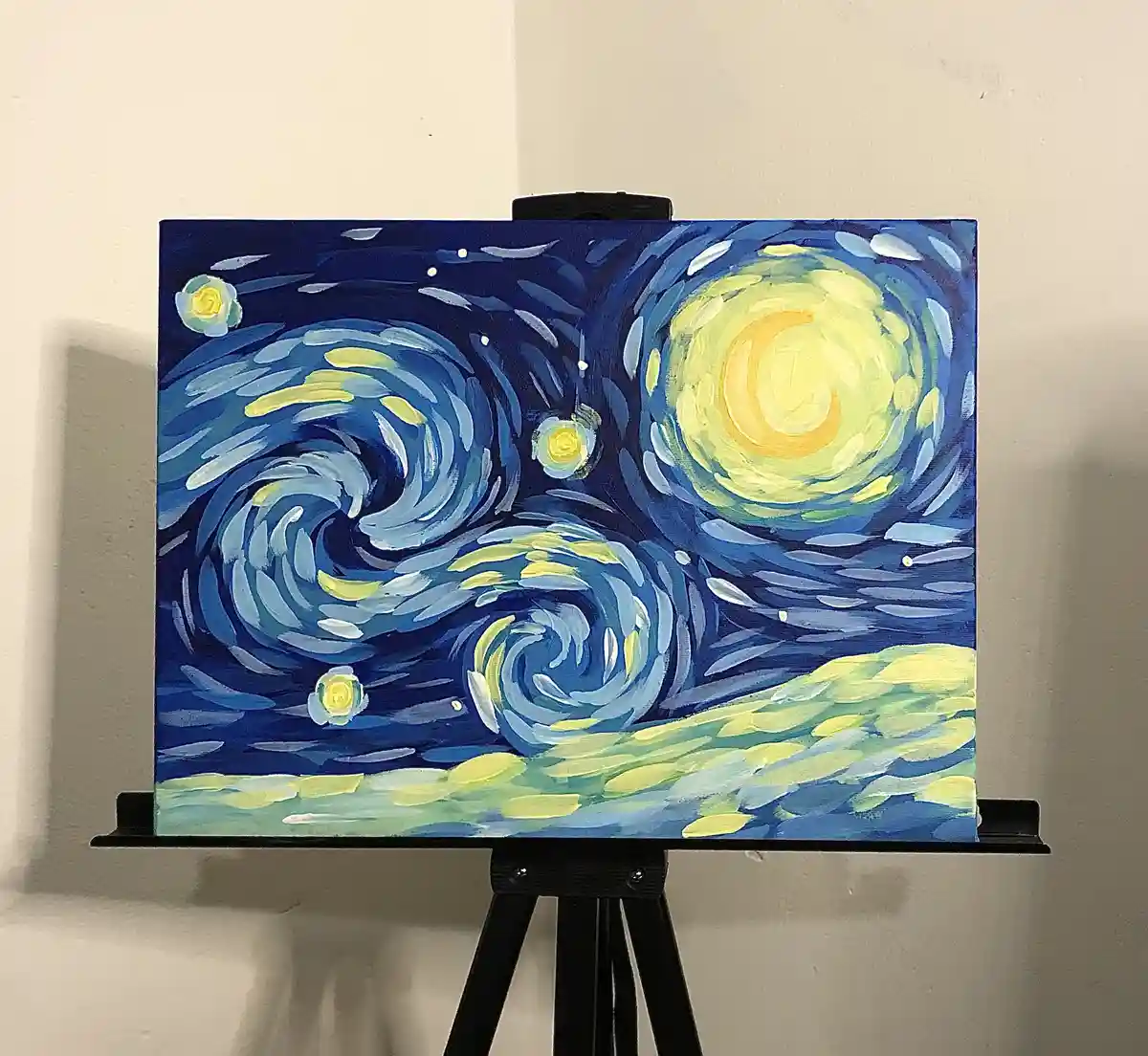 A painting of Vincent van Gogh's 'Starry Night' is displayed on a black easel against a plain wall. The artwork features a…