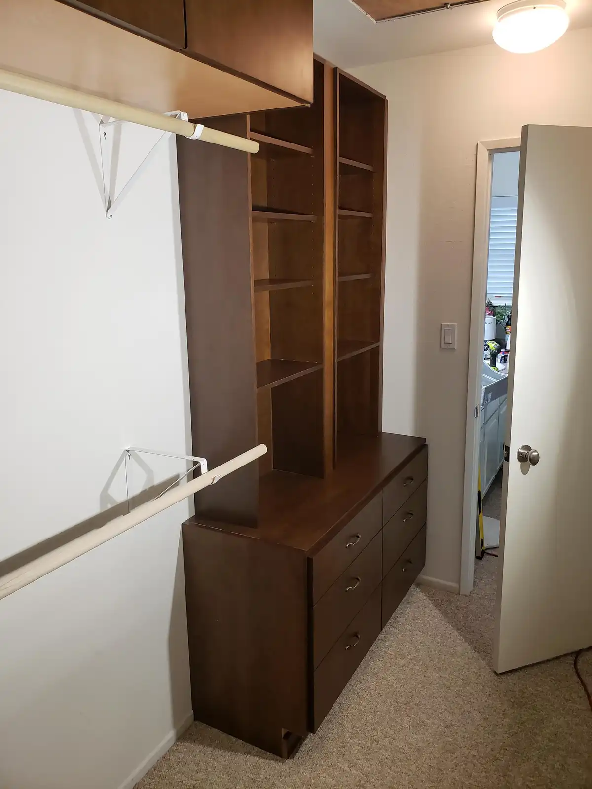 A newly installed, empty dark wood closet system with shelves, drawers, and hanging rods is shown in a room. The text…