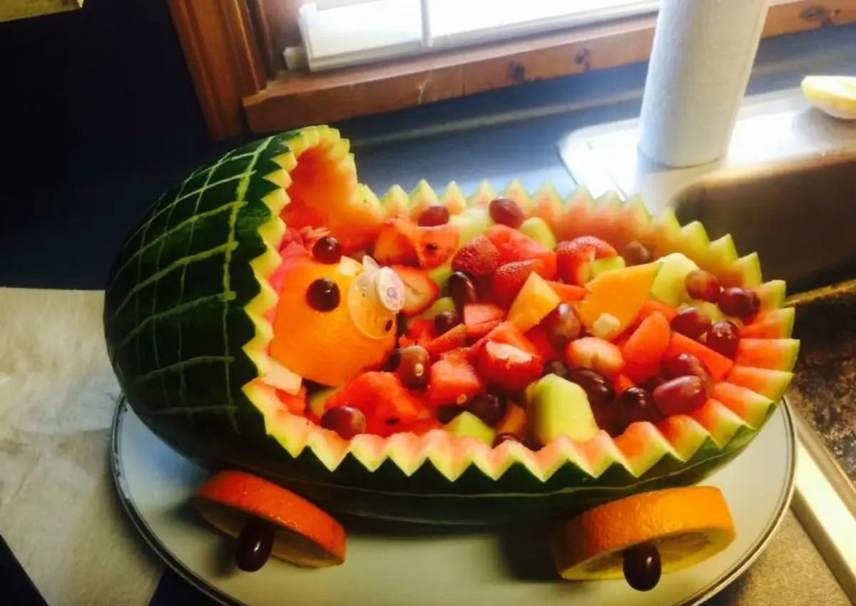 A watermelon has been carved into the shape of a baby stroller, complete with orange slice wheels and a grape 'baby' made…