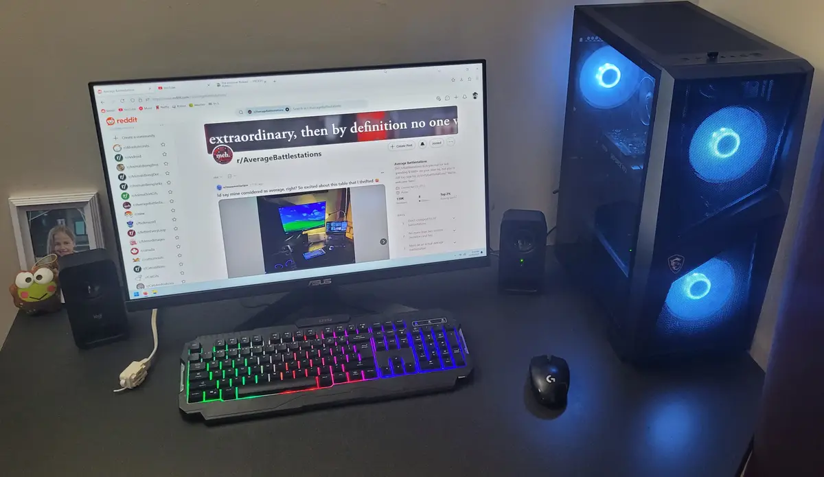 A computer desk setup with a monitor displaying the Reddit page for r/AverageBattlestations, showing a post about an…