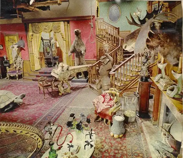 a cluttered, opulent room filled with bizarre and mismatched decor including a taxidermied moose head, a bear statue, a…