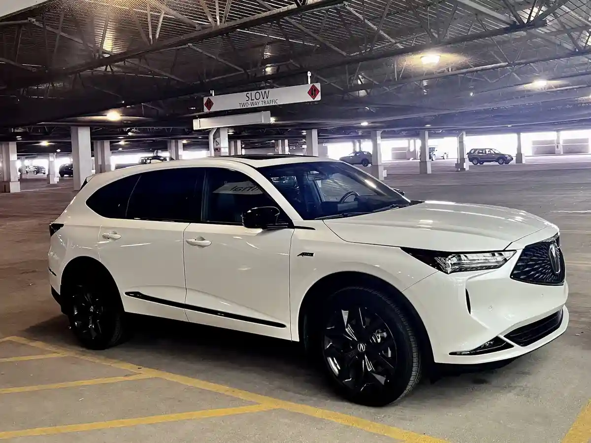 A white Acura SUV is parked in an underground parking garage, with a 'SLOW TWO-WAY TRAFFIC' sign hanging overhead. The car…