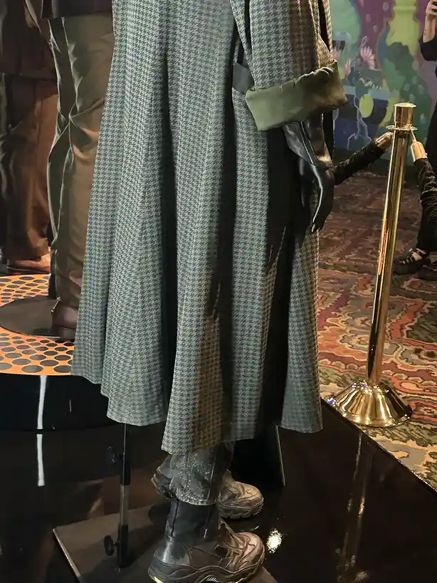 A person wearing a houndstooth-patterned coat with olive green cuffs, paired with distressed jeans and chunky black platform…