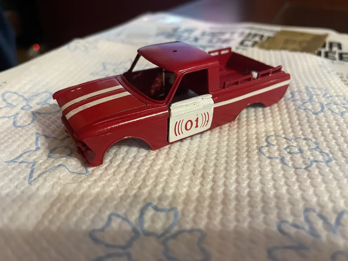 A red toy pickup truck with white racing stripes and a white door panel displaying the number '01' in red, surrounded by…