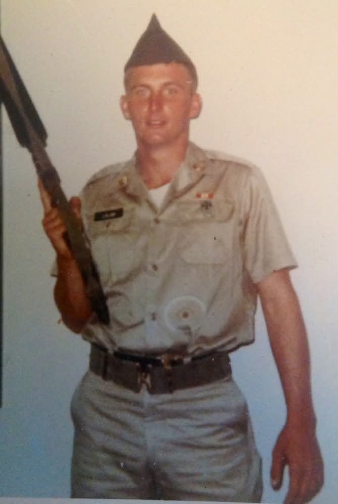A vintage photo of a young man in a military uniform holding a rifle, with a very pointed, cone-shaped cap that looks like a…