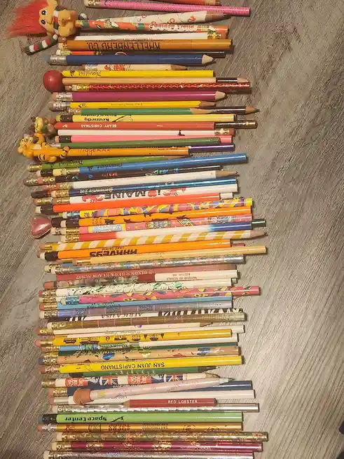 A large collection of colorful, varied pencils with different designs, logos, and erasers are arranged in a long, slightly…