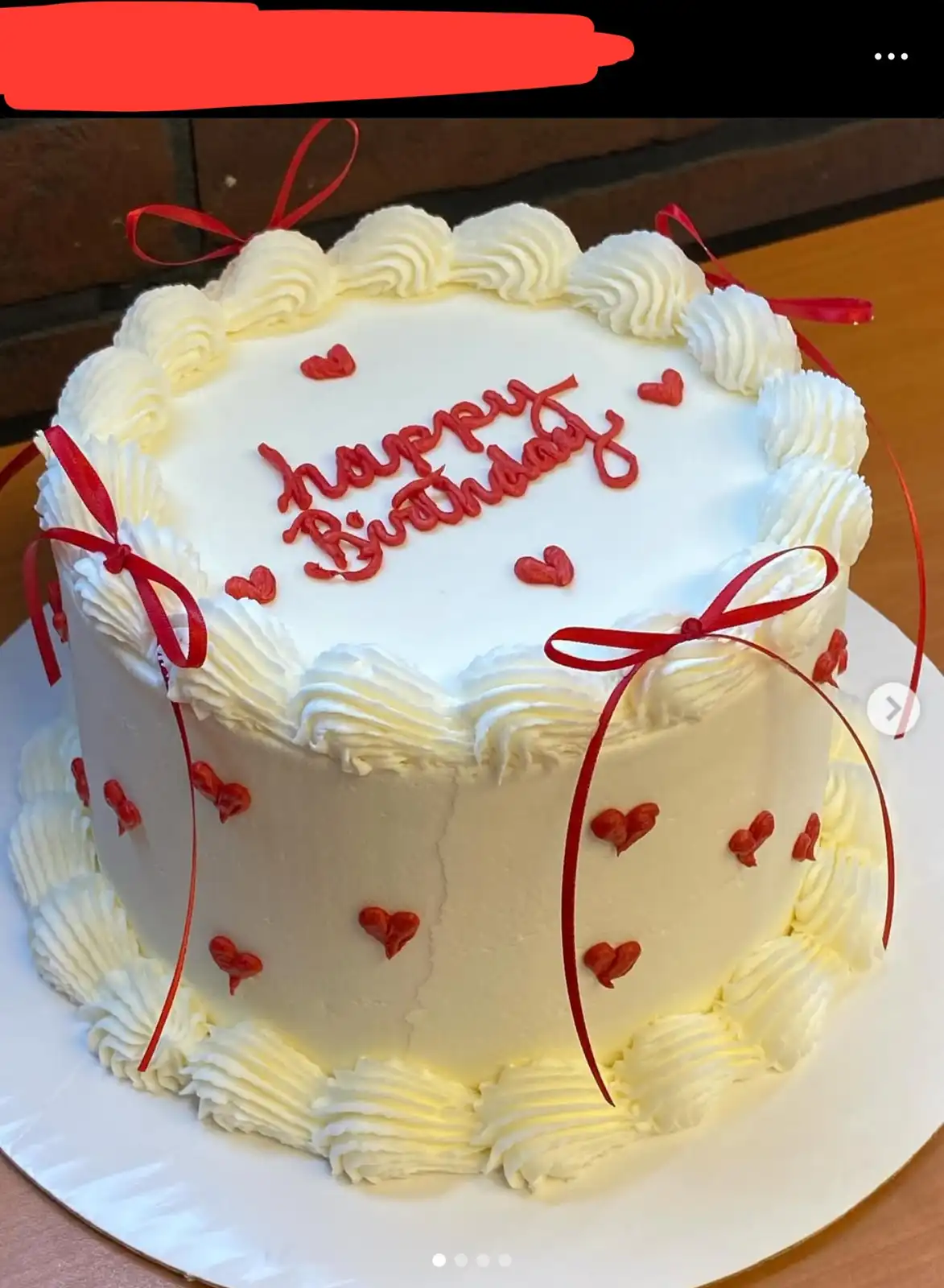 A round birthday cake with white frosting, red ribbon bows, and red heart decorations, with the text 'happy Birthday'…