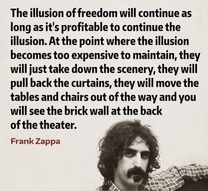 A black-and-white photo of Frank Zappa with long curly hair and a mustache, wearing a plaid shirt, looking directly at the…